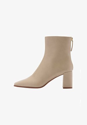Stivale in pelle beige alla caviglia con punta appuntita, texture liscia e tacco a blocco di media altezza. Caratterizzato da una cerniera laterale e un design minimalista.