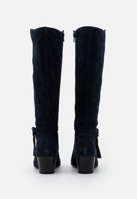 Marinblå mockakängor i knähöjd med klack, med sidodragkedjor och dekorativa snörningar runt vristerna för extra detalj.