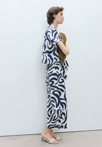 Navy and cream outfit featuring abstract swirls, loose-fit top, matching pants with tie waist, and beige slip-on sandals.