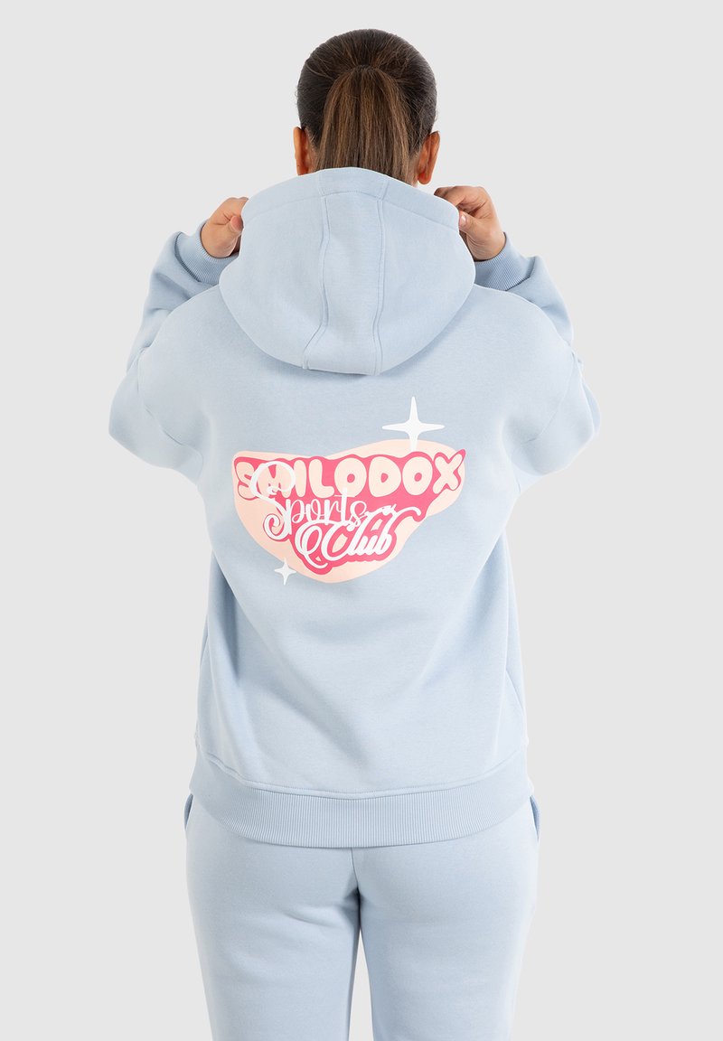 Ljusblå hoodie med en stor rosa och vit grafik "Smilodox Sports Club" på baksidan. Har en huva med snörning och ribbade manschetter.