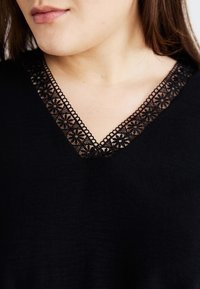 Black top featuring a V-neck with lace trim, decorated with floral patterns. The fabric has a soft, textured appearance.