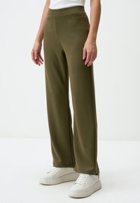 Olivgrüne, weit geschnittene Hosen aus weichem Stoff, mit hohem Bund. Kombiniert mit weißen Sneakers für einen lässigen Look.