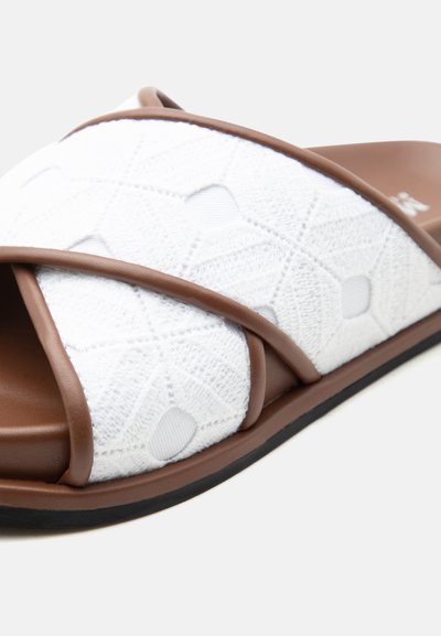 Καφέ σαγιονάρα με λευκό υφασμάτινο λουράκι με γεωμετρικά σχέδια και ανοιχτό σχέδιο δαχτύλων σε μαύρη, επίπεδη σόλα.