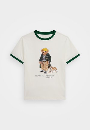 T-shirt branca com colarinho e acabamentos em verde nas mangas, apresentando uma impressão de um urso em cartoon vestido com um casaco e um cão ao seu lado.