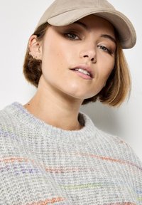 Maglione grigio lavorato a maglia con strisce multicolori, abbinato a un cappellino beige. La texture sembra morbida e accogliente, con scollatura rotonda e vestibilità comoda.