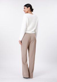 Λευκό χνουδωτό πουλόβερ με μακριά μανίκια σε συνδυασμό με ψηλόμεσα καρώ καφέ παντελόνια. Απλός σχεδιασμός, χαλαρή εφαρμογή, ομαλή υφή.