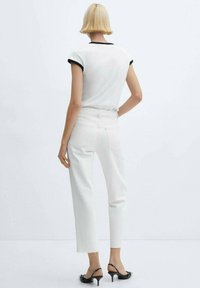 Jeans de mezclilla blancos con dobladillo sin rematar, combinados con una camiseta blanca ajustada con ribete negro en el cuello y las mangas. Vista posterior del conjunto.