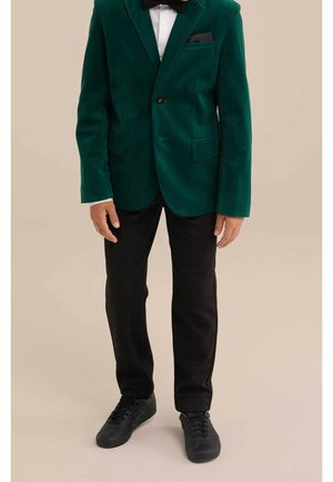 Grøn fløjlsblazer med en enkelt knap, sort lommetørklæde, parret med ternede sorte bukser og sorte sneakers.