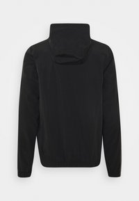 Veste noire à capuche avec manches longues vue de dos, avec poignets et ourlet élastiques sur un fond uni.