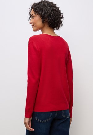 Maglione rosso con scollatura rotonda e maniche lunghe, realizzato in un materiale morbido. Indossato con jeans blu scuro, mostrato da dietro.