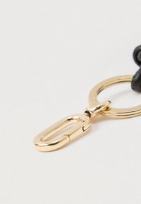 Μεταλλικό κούμπωμα σε χρυσό τόνο με κυκλικό μπρελόκ και υφασμένα μαύρα δερμάτινα στοιχεία, που διαθέτει κομψό σχεδιασμό και μηχανισμό ασφαλούς κλεισίματος.