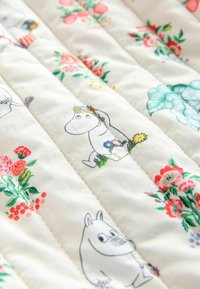 Witte geborduurde stof met kleurrijke bloemenpatronen en cartoonfiguren die lijken op nijlpaarden die bloemen dragen, gerangschikt in verticale rijen.