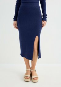 Falda de punto azul marino con una abertura lateral y detalle en el dobladillo. Combinada con sandalias de plataforma beige con correas para un ajuste seguro.