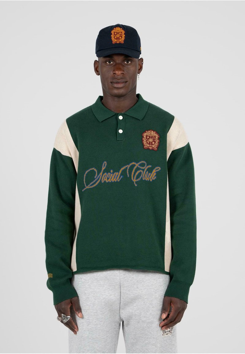 Polo a maniche lunghe verde e beige con colletto, logo ricamato e scritta "Social Club". Materiale in cotone, vestibilità rilassata, polsini a costine.