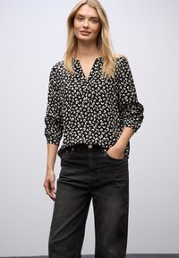Sort bluse med hvidt abstrakt mønster, v-hals, lange ermer med manchetter. Matchet med højhofte sorte jeans, begge i afslappet stil.
