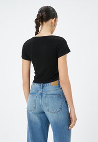 T-shirt nero a maniche corte abbinato a jeans a vita alta di colore blu chiaro, con una patch in pelle marrone sulla tasca posteriore. Tessuto dalla superficie liscia.
