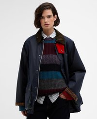 Casaco impermeável azul-marinho com colarinho de veludo cotelê, detalhes em prata e dois bolsos com aba, sobre uma camisola de malha multicolorida e uma camisa xadrez.