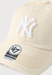 Béžová baseballová čepice s bílým vyšívaným logem "NY" a nálepkou "’47 CLEAN UP ADJUSTABLE" na zakřiveném kšilťáku.