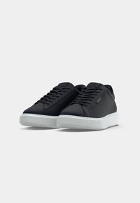 Zwarte sneakers met een zachte textielen bovenkant, platte veters en een witte rubberen zool. Eenvoudig ontwerp zonder zichtbare logo's of patronen.