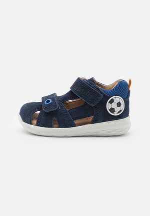 Blaue Wildledersandale mit Ausschnittdesign, doppelten Velcro-Riemen, weißer Gummisohle und einem Fußballdetail an der Seite.