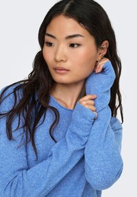 Lichtblauwe trui met lange mouwen en een losse pasvorm, met een zachte textuur en een subtiel gemêleerd patroon. Voorzien van geribbelde manchetten.