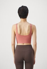 Ριγέ, κοραλλί crop top με φαρδιές τιράντες και στρογγυλή πλάτη, συνδυασμένο με ψηλόμεσα, λεία, σκούρα καφέ κολάν. Απλός σχεδιασμός, χωρίς ορατά λογότυπα.