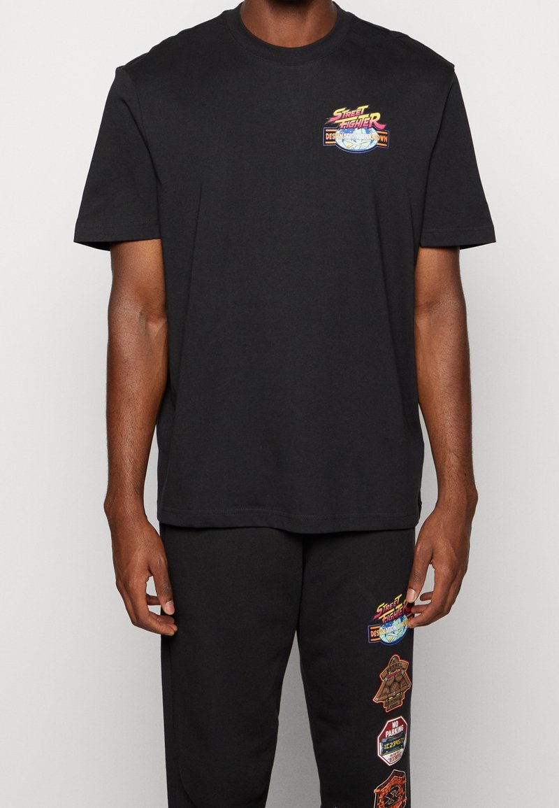 Czarna bawełniana koszulka z okrągłym dekoltem i krótkimi rękawami. Wyróżnia się kolorową grafiką "Street Fighter" na piersi. Prosty, luźny krój.