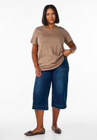 Bruine T-shirt met korte mouwen en een zak; gecombineerd met wijde donkerblauwe denim capri-broek en leoprint ballet flats.