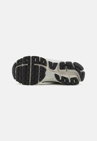 Running shoe outsole featuring a textured black rubber sole with multi-directional lugs and a grey midsole. Reinforced heel area visible.