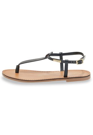 Infradito in pelle nera con suola piatta color tan. Presenta una fascetta alla caviglia regolabile e dettagli in metallo dorato sulla fascia.