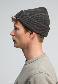 Grijze gebreide beanie met ribbeltextuur, spitse bovenkant, dicht op het hoofd gedragen, gecombineerd met een lichtgrijze sweatshirt. Eenvoudig ontwerp, zonder versieringen.