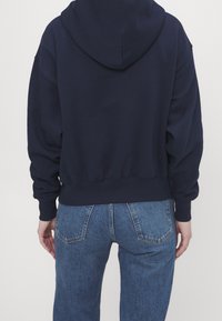 Felpa con cappuccio blu navy dal taglio ampio, polsini e orlo a costine, tessuto morbido, abbinata a jeans denim azzurri.