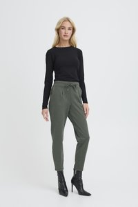 Černý top s dlouhým rukávem v kombinaci se zelenými jogger kalhotami se stahovacími šňůrkami v pase, bočními kapsami a zúženými nohavicemi, obutý s černými botami na podpatku.
