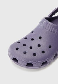 Purple clog made of lightweight plastic, featuring circular ventilation holes, a textured surface, and cut-out heel straps for easy wear.