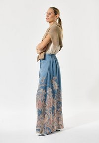 Lichtblauwe maxi rok met bloemenborduursel in roze en beige, gecombineerd met een beige gebreide sjaal en een crèmekleurige top. Beschikt over een trekkoord in de taille.