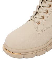 Beżowe skórzane botki za kostkę z teksturowanym wierzchem, okrągłym noskiem i złotym akcentem na podeszwie. Posiadają klasyczny fason na sznurówki oraz solidny bieżnik.