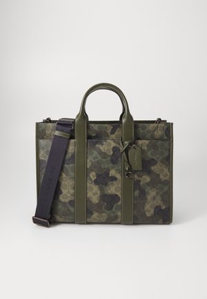 Sac fourre-tout à motif camouflage avec poignées en cuir vert, sangles verticales et une bandoulière noire ajustable avec une étiquette pendante.