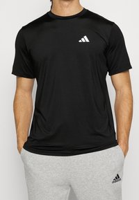 Camiseta atlética negra de manga corta con cuello redondo y un logo blanco de Adidas en la parte izquierda del pecho. Fabricada con tejido ligero.