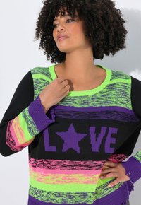 Pull en tricot avec des rayures vertes vives, noires et violettes, arborant le texte "LOVE" et un motif d'étoile, reconnu pour sa texture douce et sa coupe décontractée.
