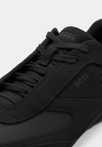 Czarny sneaker na sznurowadła z teksturowanej tkaniny i gładkimi panelami, z wytłoczonym logo "BOSS" na języku i boku.