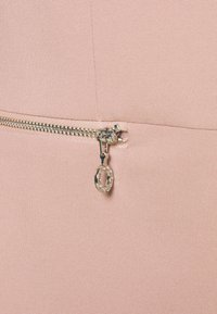 Světle růžová tkanina s hladkým povrchem, která má stříbrný zip. Stahovák zipu má kulatý přívěsek zdobený průhlednými kamínky.