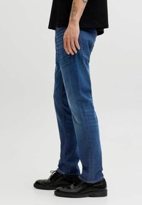 Tumesinised teksapüksid, millel on sirge sääre disain, peened pleekimised ja aksentõmblused. Ühildatud mustade paeltega kingadega.