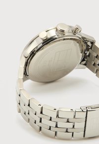 Ασημί αδιάβροχο ρολόι χειρός από ανοξείδωτο ατσάλι με μπρασελέ από μεταλλικούς κρίκους, ορατή πίσω πλευρά και τρία κουμπιά ελέγχου στο πλάι.