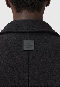 Zwart wollen jasje met een gestructureerde afwerking, voorzien van een notch-kragen en een rechthoekig leren label met "ALLSAINTS LONDON" aan de achterkant.