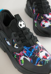 Black athletic shoes with a colorful soccer ball graphic, textured upper, and black laces. Features a prominent soccer ball button accent.