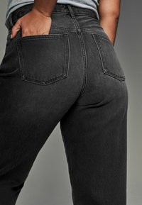 Jeans de mezclilla negra que muestran los bolsillos traseros, diseño de cintura alta y una textura suave. Costuras visibles que acentúan los bolsillos y las costuras.