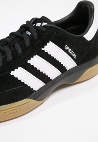 Black suede sneaker with white leather stripes, textured surface, rubber sole, and "SPEZIAL" branding on the side. Classic athletic design.