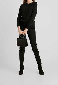 Sweat-shirt noir avec des détails texturés aux épaules, pantalon noir à coupe slim, et petit sac à main avec une anse circulaire et une fermeture à rabat.