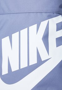 Kék szövet, textúrált felülettel, nagy fehér "NIKE" logóval és swoosh dizájnnal büszkélkedik, létrehozva ezzel egy merész, grafikai megjelenést.