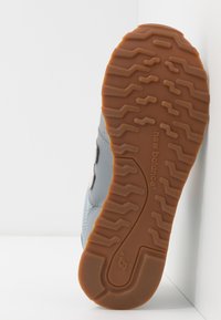 Zapatilla gris con suela de goma, patrón de tracción texturizado y acento de logo. Cuenta con materiales superiores de cuero y malla.